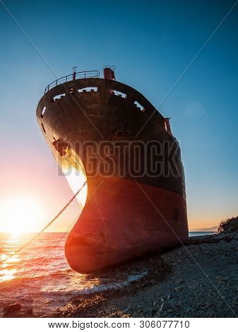 Large Iron Cargo Ship Run Aground At Sea Bay At Sunset. Industrial Sea Vessel Shipwreck On Coastline