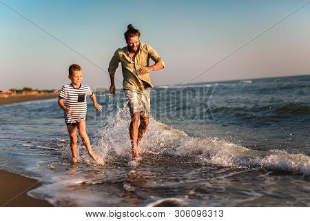Happy Father And Son, Man & Boy Child, Running And Having Fun In The Sand And Waves Of A Sunny Beach