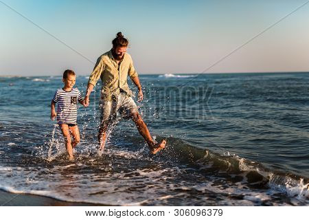 Happy Father And Son, Man & Boy Child, Running And Having Fun In The Sand And Waves Of A Sunny Beach