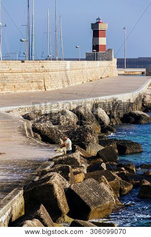 Monopoli, Italy - July 6 2018: Man Fishing In Front Of Lighthouse In Monopoli Port Near Castle Of Ca