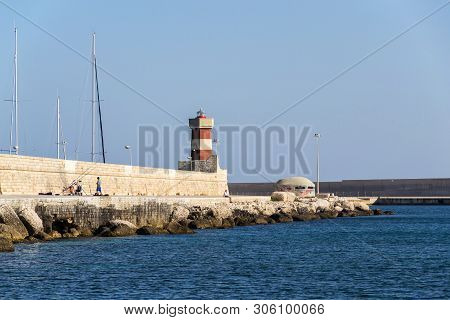 Monopoli, Italy - July 6 2018: Man Fishing In Front Of Lighthouse In Monopoli Port Near Castle Of Ca