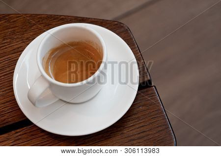 Italian Espresso In A White Ceramic Cup With Saucer On A Brown Wood Table. Brurred Background.