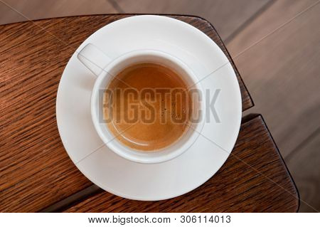 Italian Espresso In A White Ceramic Cup With Saucer On A Brown Wood Table From Above. Brurred Backgr