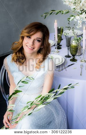 Sitting Bride With Olive Branch In Hands  And Wedding Decorations For Banquet With Sakura, Candles A
