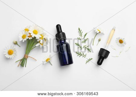 Composition With Chamomile Flowers And Cosmetic Bottle Of Essential Oil On White Background, Top Vie
