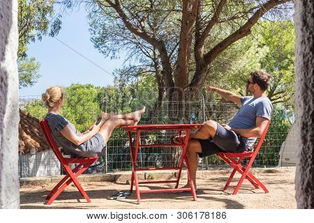Couple On Vacations Resting In Front Of Bungalow House At Camping Site In Pure Nature. Family Vacati