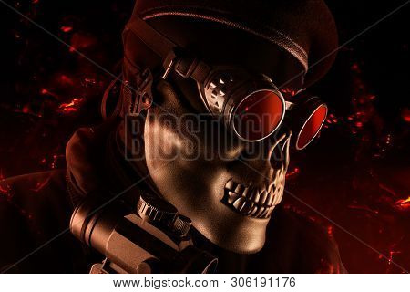 Photo of a fully equipped soldier in black armor tactical vest standing in skull mask and beret on black background with flying ashes closeup angle view.