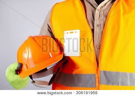 Photo of a worker in orange jacket outfit with gloves holding protective orangle helmet closeup torso view on grey background.