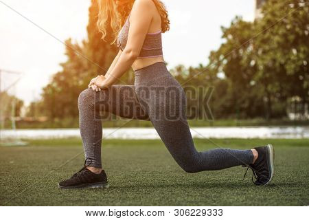 Close-up Female Legs In Sports Leggings And Black Sneakers. Girl With Wavy Blond Hair Is Doing Half-