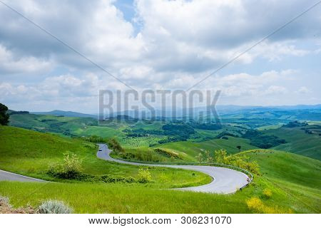 Picturesque Tuscany landscape with rolling hills, valleys, sunny fields, cypress trees along winding rural road, houses on a hill. Tourist visit in Tuscany 