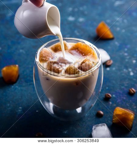 Ice Coffee With Milk In A Modern Glass With A Double Bottom Next To The White Creamer On A Blue Back