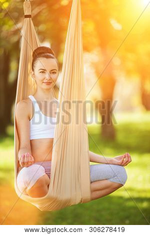 Anti-gravity Yoga outdoor. Happy woman doing yoga exercises, meditate in the park. Yoga meditation in hammock. Concept of healthy lifestyle and relaxation. Pretty woman relax at yoga hammock