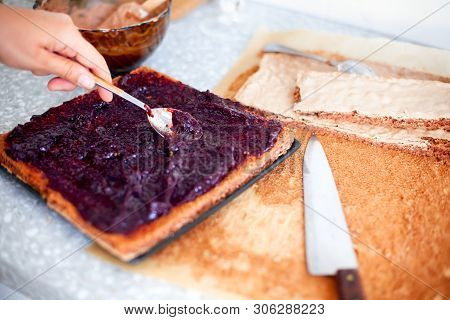 Woman Making Cake. Person Hand With Spoon Spreads Jam On Sponge Cake On Domestic Kitchen.