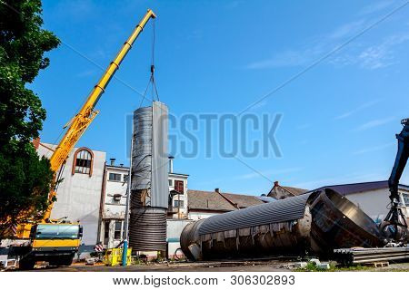 Crane Is Bringing Down Heavy Metal Silo In Industrial Complex.
