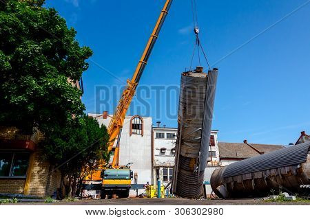 Crane Is Bringing Down Heavy Metal Silo In Industrial Complex.