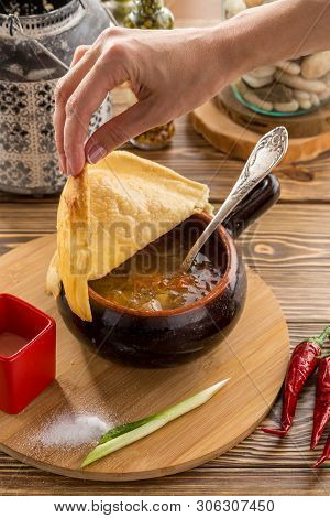 Female Hand Holding Bread Lid On Russian Cabbage Soup Shchi With Beef In Clay Pot On Wooden Table Si