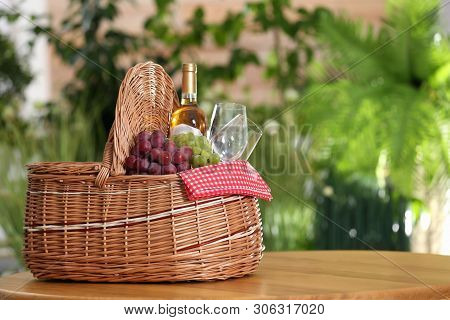 Picnic Basket With Wine, Glasses And Grapes On Wooden Table Against Blurred Background, Space For Te