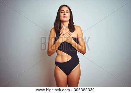 Beautiful woman wearing bikini swimwear over white isolated background smiling with hands on chest with closed eyes and grateful gesture on face. Health concept.
