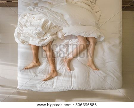Top View Of Romantic Couple Sleeping. Bare Feet Of Their Legs Lying In A Bed With White Blanket In L