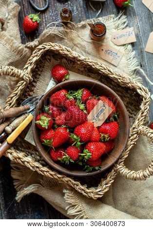 Overhead Shot Of Tasty Ripe Strawberries In Wooden Bowl Stands In Wicker Strawy Basket On Rustic Tab