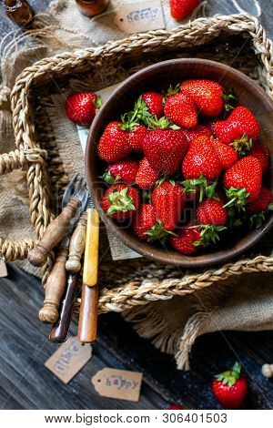 Overhead Shot Of Tasty Ripe Strawberries In Wooden Bowl Stands In Wicker Strawy Basket On Rustic Tab