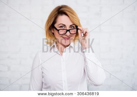 Portrait Of Cheerful Mature Business Woman In Eyeglasses Posing Over White Brick Wall