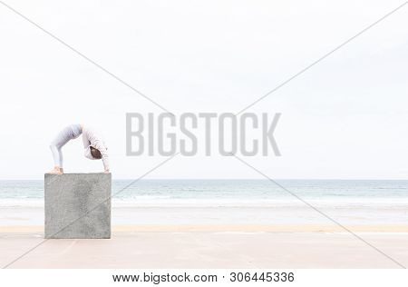 Woman Yogi Doing The Pigeon Pose On A Stone Cube On The Beach With The Sea In The Background