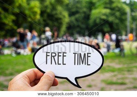 closeup of the hand of a young caucasian man holding a signboard, in the shape of a speech bubble, with the text free time written in it, in a public park