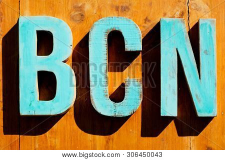 pale blue wooden three-dimensional letters forming the text BCN, an abbreviation for Barcelona, Spain, on a wooden background