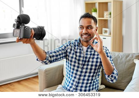 blogging, videoblog and people concept - smiling indian male video blogger with camera videoblogging making ok gesture at home