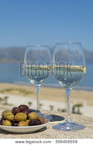Two Wine Glasses With White Wine Served With Olives On Outdoor Terrace Witn Blue Sea And Mountains V