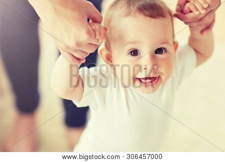family, child, childhood and parenthood concept - close up of happy little baby learning to walk with mother help at home