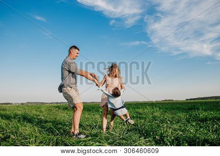 Mother And Father Swinging Son In Sunnny Summer Day