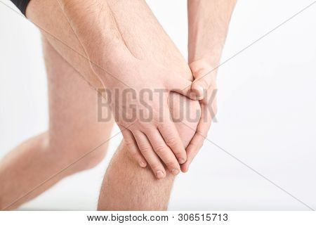 A Man In Underwear Holds His Knee With A Hand On A Gray Background.
