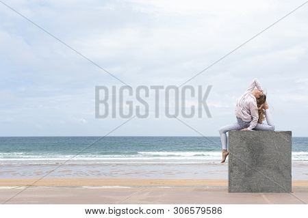 Woman Yogi Doing The Pigeon Pose On A Stone Cube On The Beach With The Sea In The Background
