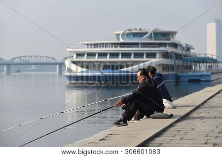 Pyongyang, North Korea - May 1, 2019: Street Scene. Two Fishermen Catch A Fish On Waterfront On  Kim