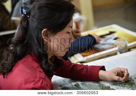 Pyongyang, North Korea - April 29, 2019: Girl Factory Worker With Needle And Silk Thread Over Canvas