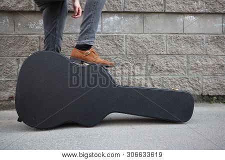 Man Put His Foot On A Hard Guitar Case. Hard Case For Electric Guitar. Man Dressed In Jeans Holding 