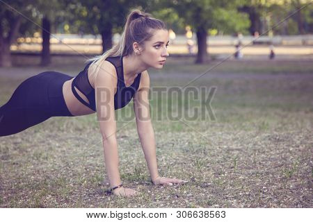 A Young Woman Engaged In Crossfit In The Park. Doing Push-up