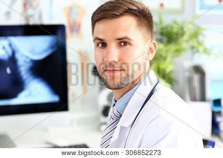 Portrait Of Smart Physician Sitting In Clinic Cabinet. Doc Surgeon Posing In White Uniform. Medical 