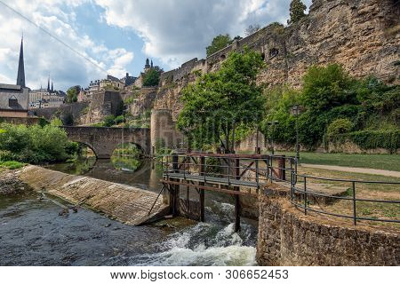 Weir In Alzette River Luxembourg City Downtown Grund With Medieval Fortifications And Old Stonebridg