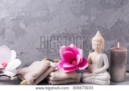 Decorative Buddha And Pink Magnolia Flowers, Towels And Burning Candle On Grey Textured Background. 