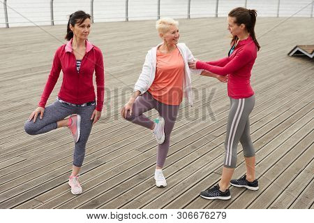 Full Length Portrait Of Three Senior Women Doing Yoga On Pier During Outdoor Class In Morning, Copy 