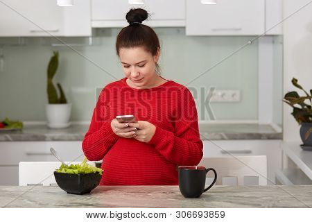 Image Of Amazing Healthy Pregnant Woman In Kitchen At Home Using Mobile Phone For Checking Social Ne