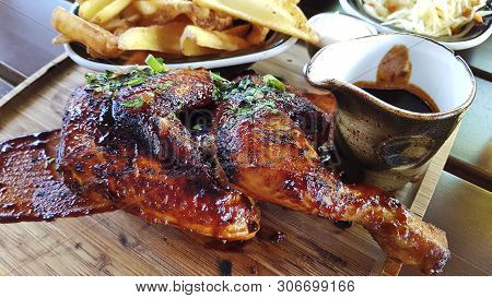 Half Of The Fried Chicken Is Served On A Wooden Tray. On A Tray Fried Potatoes And Sauce. Finely Cho