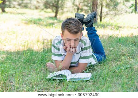 The Boy Lies In The Park On The Grass And Is Studying In Nature, Education And Science, The Book Is 