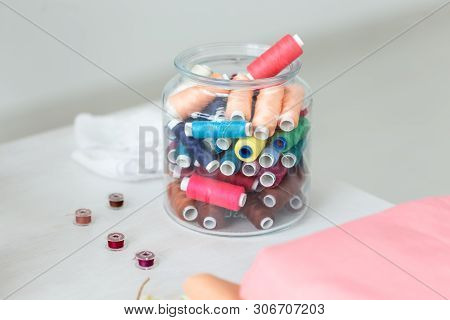 Close Up Multicolored Threads And Bobbins Lie On A Table In A Transparent Glass Jar On The Seamstres