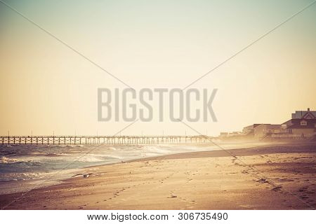 A Long Fishing Pier Heading Out Into The Distance On The Horizon With Ocean Waves Crashing On The Be