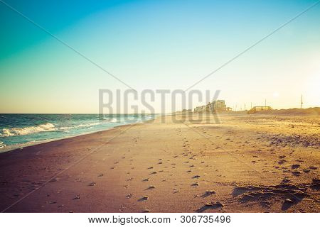 Foot Prints In The Sand Leading Away Form The Viewer On A Long Sandy Beach In Evening Light.