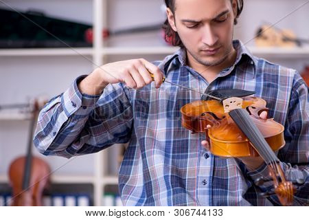 Young handsome repairman repairing violin